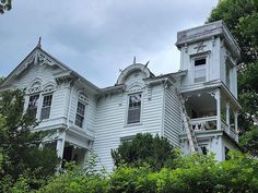 an old white house with many windows and balconies on the second story is surrounded by greenery