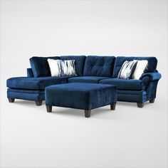 a blue sectional couch and ottoman with pillows on the bottom, in front of a white background