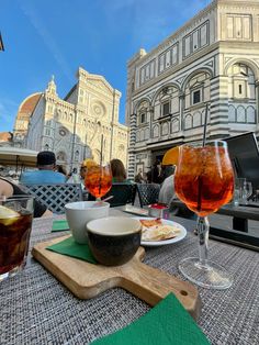 two glasses of wine are sitting on a table with food and drinks in front of them