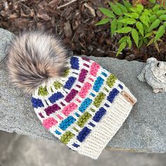 "This fun, multi-colored Draughts Beanie was hand knit by me with several colors of Malabrigo Chunky wool. The fit is fabulous & sized to fit most adult heads up to 22\" in circumference. Hat is topped with a luxury faux fur pom which is tied on using an engraved wood pom button. Care instructions: remove pom & spot clean or hand wash in mild soap. Roll in towel - do not wring - to remove excess water. Lay flat to dry. Pom can be refluffed with a blow dryer - just don't touch the heating element directly to the faux fur. Pattern for the Draughts Beanie was designed by Canadian, Cate Savard of Weird Sheep. Thank you for supporting my small business!" Crochet Beanie Patterns With Yarn, Crochet Beanie Patterns In Yarn, Multicolor Knitted Beanie For Cold Weather, Multicolor Knitted Hats For Cold Weather, Hand Knitted Multicolor Crochet Hat In Yarn, Winter Crochet Patterns With Yarn, Multicolor Knit Crochet Hat, Multicolor Knitting Patterns In Yarn, Multicolor Crochet Knitting Pattern One Size