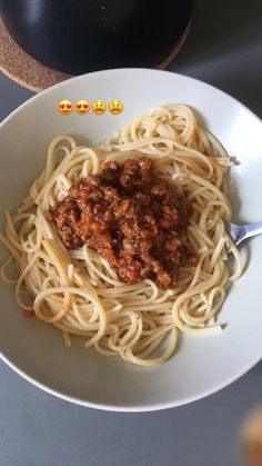 a white bowl filled with spaghetti and meat sauce next to two emoticive smiley faces