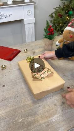 a person cutting up a cake on top of a wooden table next to a christmas tree