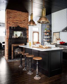 a kitchen with an island and stools next to a fireplace in the middle of it