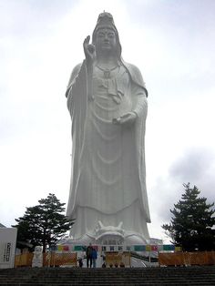 a large white statue sitting in the middle of a park next to stairs and trees