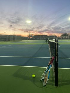 two tennis rackets leaning against a pole on a court at sunset or dawn with the sun setting in the background