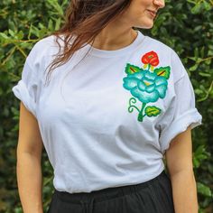 White T-shirt with Hand-Embroidered Flowers Made in Oaxaca, Mexico This white t-shirt is transformed into a piece of art with the famous Oaxacan flower hand-embroidered on the left chest. Each flower is different in color and shape, making each shirt unique. The bright embroidery stands out against the white background, making it a focal point of any outfit. These "flores istmeñas" are designed and transferred onto the fabric, then stretched on a frame for the intricate chain stitch embroidery. Each flower can take up to a week to complete, reflecting the artisan's dedication. Perfect for an effortless, sophisticated look, this t-shirt pairs well with jeans, skirts, or trousers. It's a stunning blend of modern fashion and traditional craftsmanship. Made in Juchitan de Zaragoza, Oaxaca Hand White Floral Embroidered T-shirt, White Short Sleeve T-shirt With Floral Embroidery, White Floral Embroidery Short Sleeve T-shirt, White Floral Embroidered Short Sleeve T-shirt, White Crew Neck T-shirt With Floral Embroidery, White T-shirt With Machine Embroidery, Short Sleeve, White Crew Neck T-shirt With Floral Applique, White Short Sleeve T-shirt With Floral Applique, Traditional Embroidered Summer T-shirt