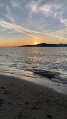 the sun is setting at the beach with footprints in the sand