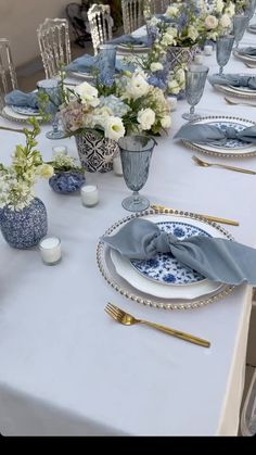 the table is set with blue and white plates, silverware, and vases