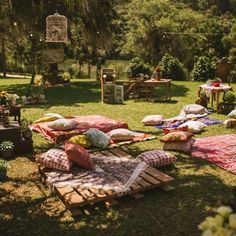 an outdoor picnic area with lots of pillows and blankets on the grass, in front of a tree