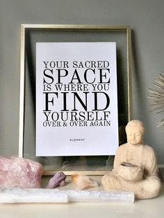 a buddha statue sitting next to a framed print with the quote your sacred space is where you find yourself over and over again