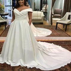 a woman standing in front of a mirror wearing a wedding dress with an off the shoulder neckline