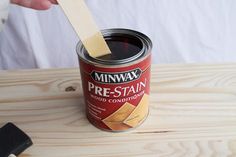 a person holding a wooden spatula over a can of paint on top of a table