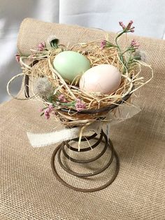 three eggs are in a nest on a stand with flowers and twine around it