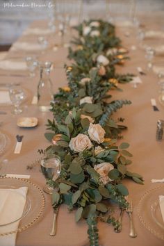 a long table with flowers and greenery on top of it, along with place settings