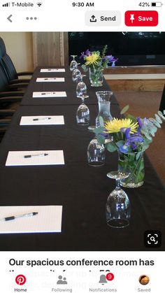 a long table with several vases filled with flowers and writing paper on top of it