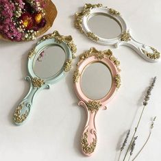 three different colored mirrors sitting next to each other on a white table with flowers in the background