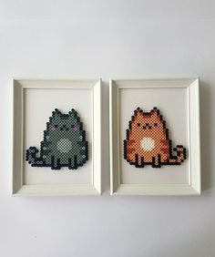 two framed cross stitch cats sitting next to each other on a white wall with one cat in the middle