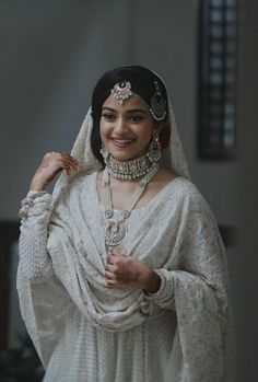 a woman in a white wedding dress and jewelry smiles at the camera while posing for a photo