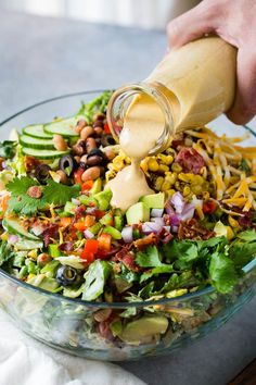 someone pouring dressing onto a salad in a glass bowl