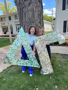 two girls are posing in front of a large letter made out of mosaic glass tiles