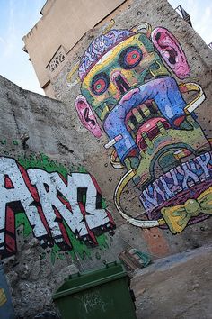 graffiti on the side of a building with a green trash can in front of it