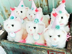 a group of white stuffed animals wearing party hats in a wooden crate with pink ribbon