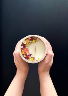 two hands holding a white candle with flowers in it