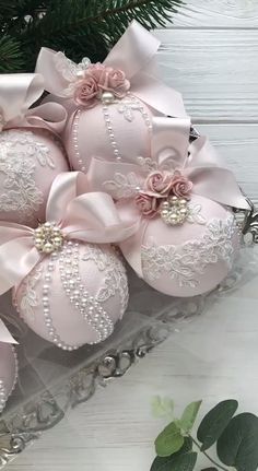 pink christmas ornaments in a glass box with ribbon and bows on the top, sitting next to a pine tree