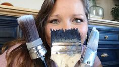 a woman holding two paint brushes in front of her face, and another brush behind her