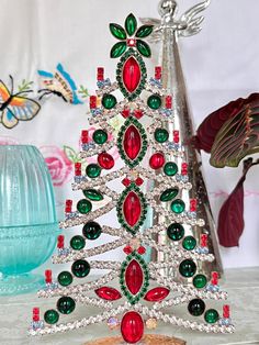 a small christmas tree made out of glass beads and other jewels on a table next to a vase