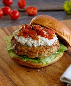 a chicken burger with tomatoes and lettuce on a wooden cutting board next to cherry tomatoes