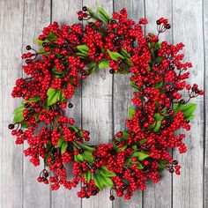 a wreath with red berries and green leaves hanging on a wooden wall next to a fence