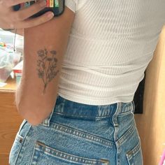 a woman with a flower tattoo on her arm holding a cell phone in her hand