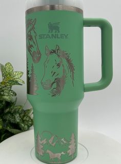 a green travel mug sitting on top of a white table next to a potted plant