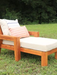 a wooden chair sitting in the grass with pillows on it's back and arms