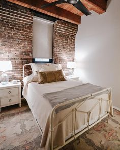 a bedroom with brick walls and white bedding, two night stands on either side