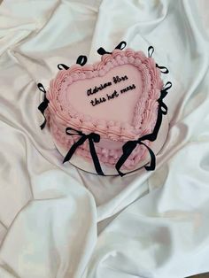 a pink heart shaped cake on top of a white sheet covered tablecloth with black ribbon