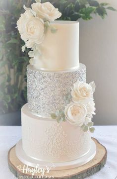 a three tiered wedding cake with white flowers on top and silver sequins