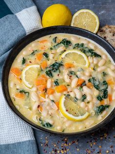 a bowl of white bean soup with lemons, spinach and bread on the side