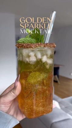 a person holding up a glass with ice and mint in it that says golden sparkle cocktail