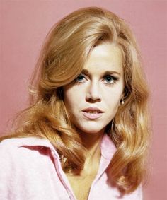 a woman with long blonde hair and blue eyes posing for a photo in front of a pink background