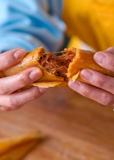 a person holding a sandwich in their hands with meat on it and cheese on the inside