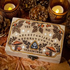 a wooden box sitting on top of a pile of leaves next to candles and pine cones