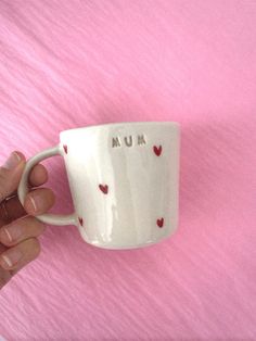 a hand holding a coffee cup with hearts on it and the word mum written in small letters