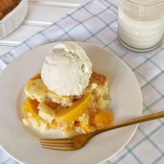 a white plate topped with an ice cream and fruit cobbler next to a glass of milk