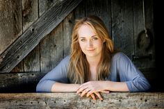 a woman leaning on a wooden ledge in front of an old barn door with her arms crossed