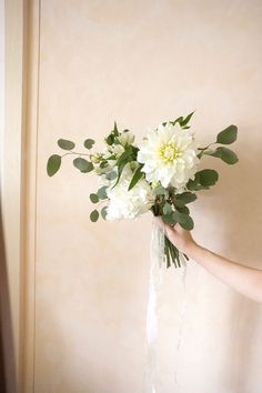 a woman holding a vase with flowers in it and greenery on the bottom half