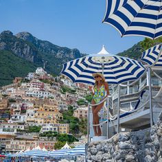 a woman standing under an umbrella on the beach in front of some buildings and mountains