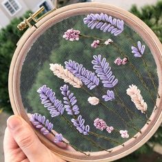 a person holding up a cross - stitch pattern with purple flowers on the inside of it