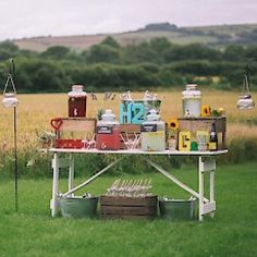 a picnic table with food and drinks on it in the middle of a grassy field